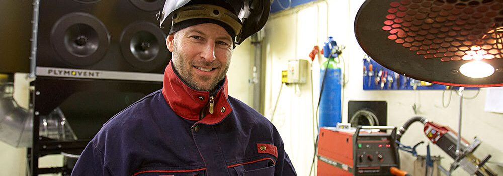 A man in a work shop smiling with protective gear on.
